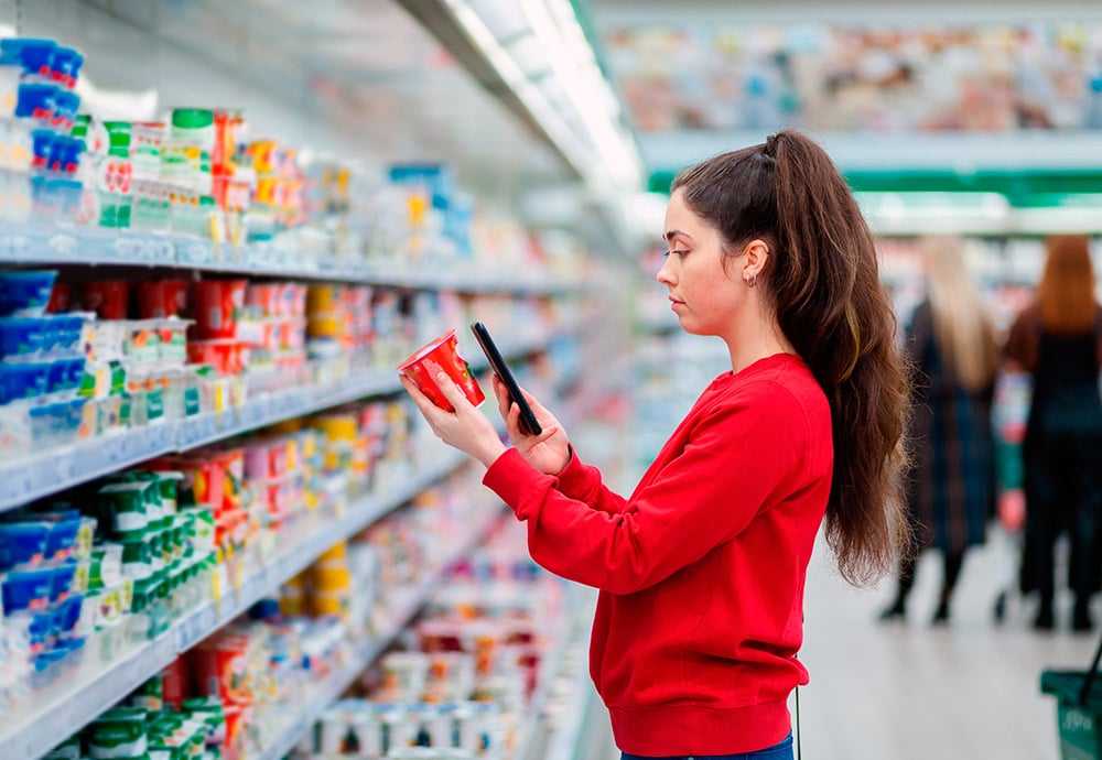Mujer joven con jersey rojo comprueba el valor nutricional de un producto lácteo a través de una aplicación del teléfono móvil.