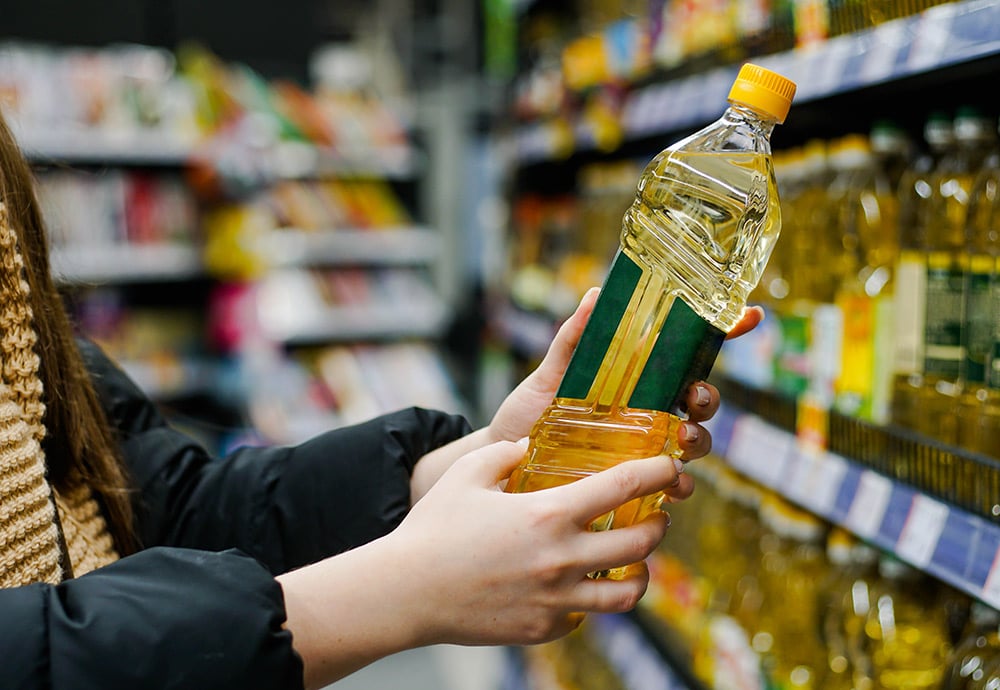 Manos de una mujer sosteniendo una botella de aceite de girasol en un supermercado.