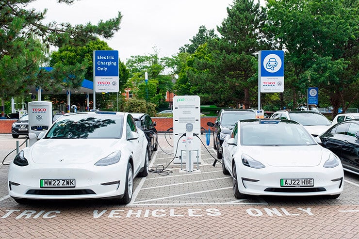 Coches Tesla blancos aparcados y enchufados en unos cargadores situados en un parking público.