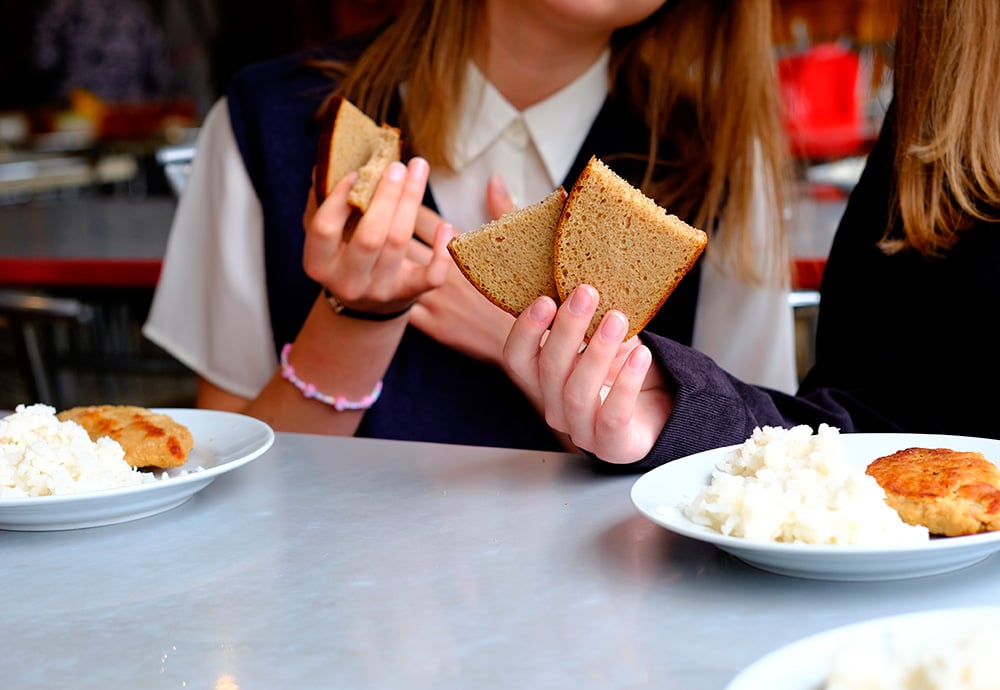 Colegialas sostiene rebanas de pan de molde en un comedor escolar. 
