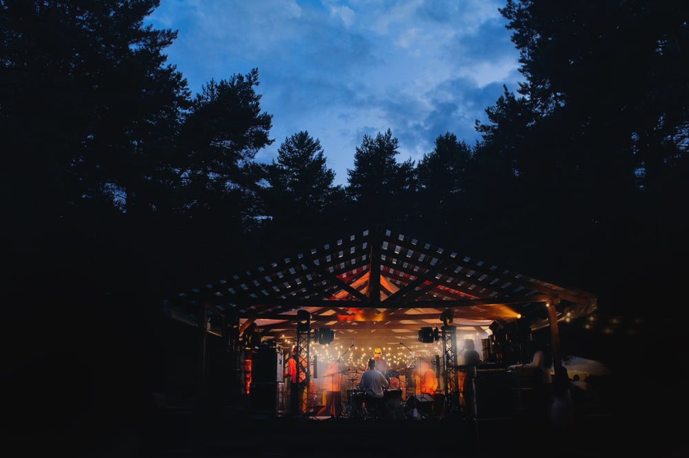Una banda de música toca en un escenario de madera en medio de un bosque.