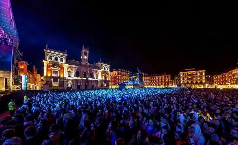 Multitud de personas disfrutando de un concierto nocturno en la Plaza Mayor de Valladolid, con los edificios iluminados y el Ayuntamiento al fondo.