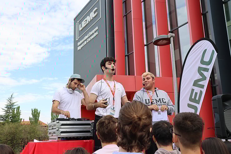 Miembros de la organización de la Jornada de Bienvenida de la UEMC, subidos a un escenario y con un DJ de fondo, se dirigen a los asistentes.