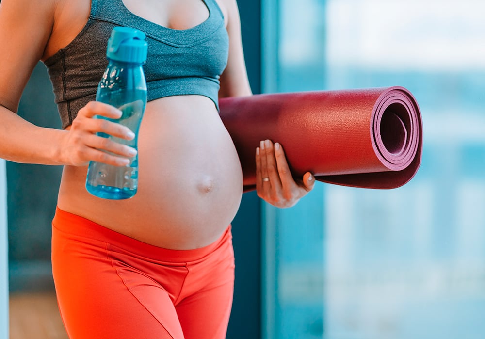 Torso de mujer embarazada sosteniendo con una mano una botella de agua y con la otra una esterilla.