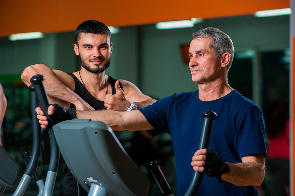 Entrenador supervisando a adulto mayor durante ejercicio en máquina elíptica