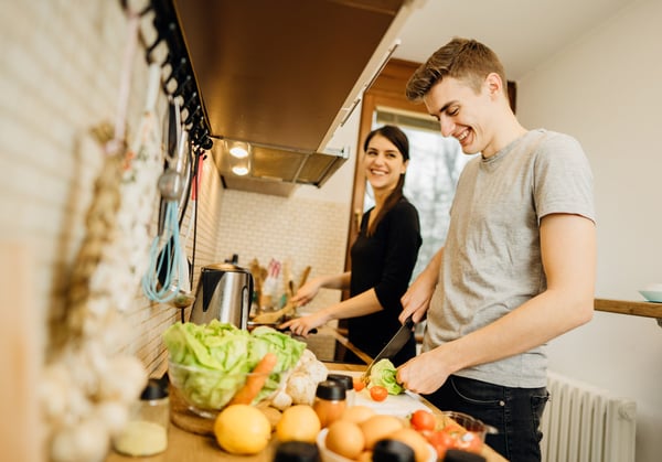 Una pareja de estudiantes sonríen mientras cocinan durante el confinamiento