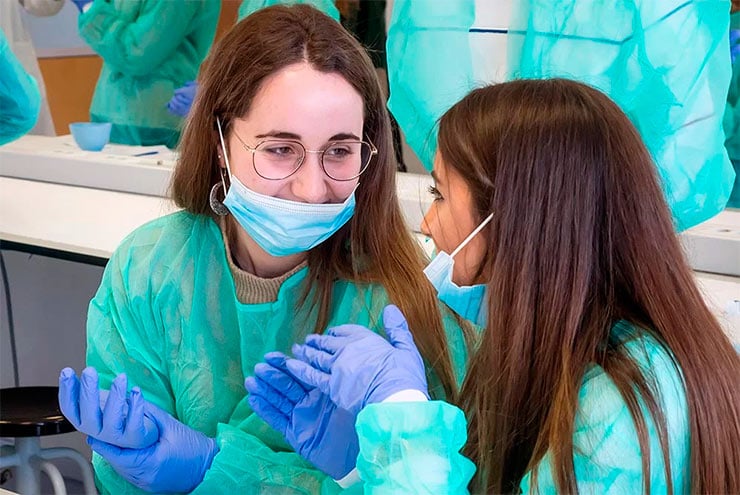 Dos futuras estudiantes se miran sonrientes tras vestirse con un EPI destinado a las prácticas en la Clínica Odontológica de la UEMC  