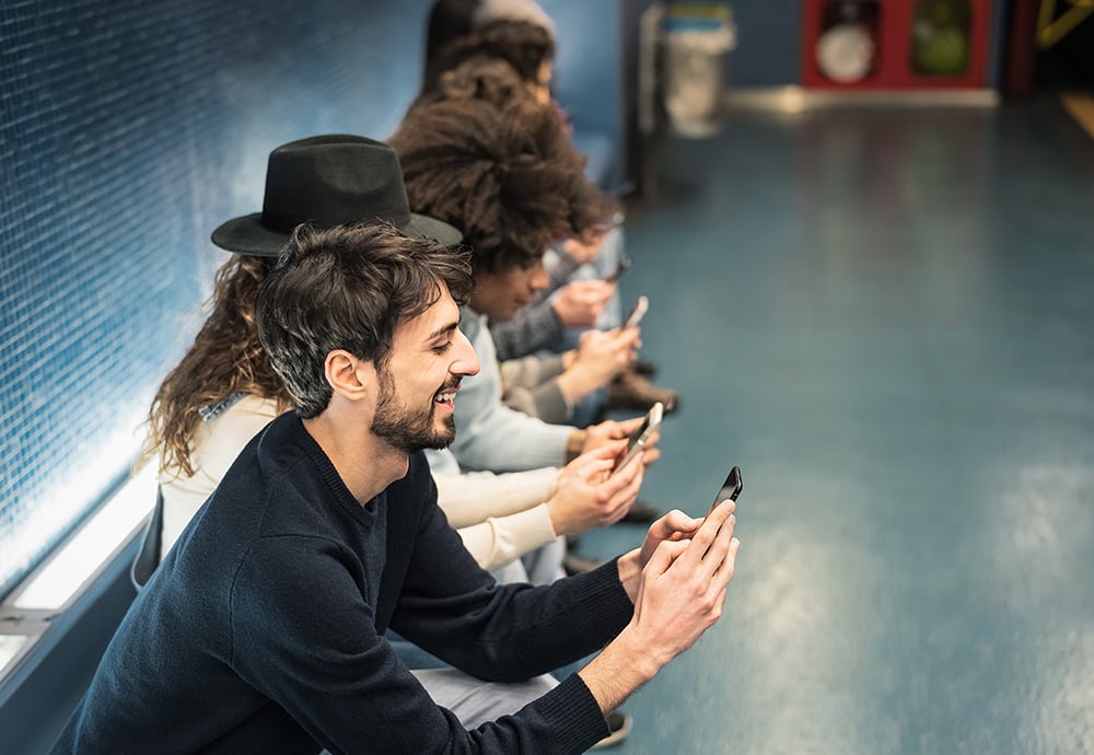 Grupo de jóvenes sentados en un banco de una estación utilizando sus teléfonos móviles.