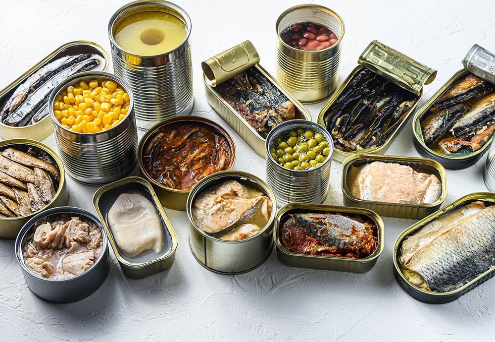 Un conjunto de conservas abiertas en las que se ven aceitunas, atún, maíz, frijoles, sardinas…