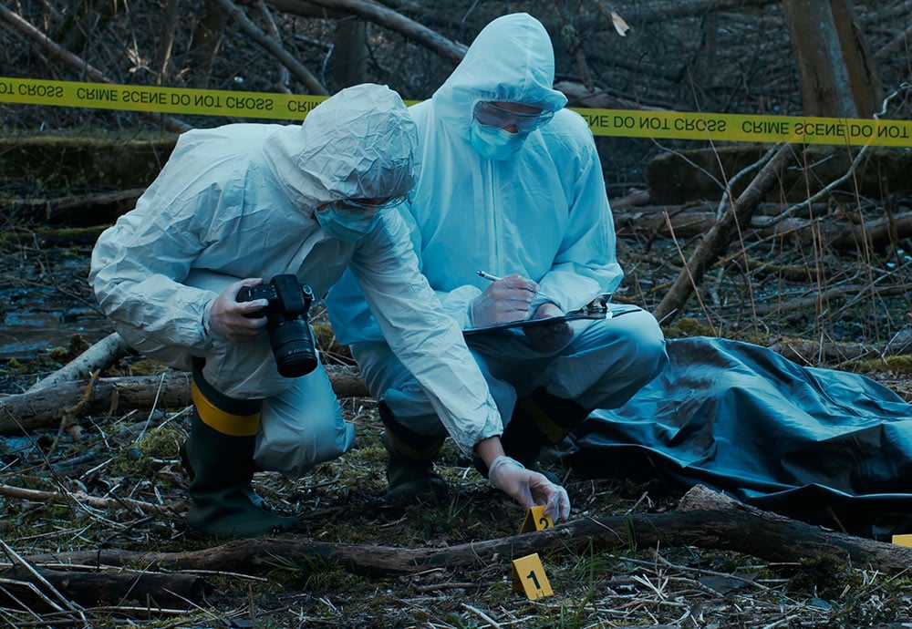 Forenses de la policía científica inspeccionan la escena de un crimen en un bosque.