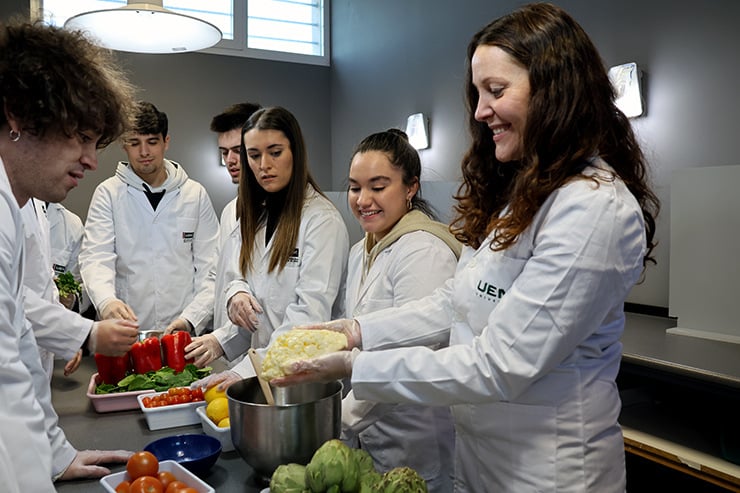 Una profesora de la UEMC enseña a estudiantes del grado en Nutrición, todos ellos con batas blancas, una masa blanca elaborada en un laboratorio.