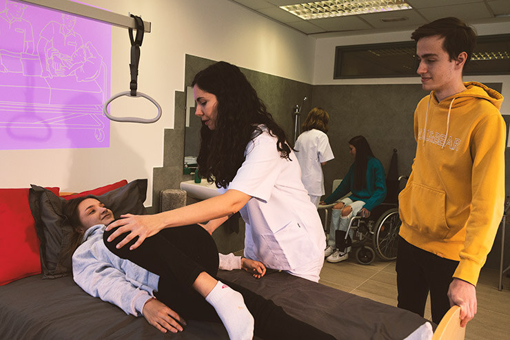 Una profesora del grado en Terapia Ocupacional de la UEMC enseña a un alumno cómo hacer un movimiento a un paciente acostado en una cama adaptada.