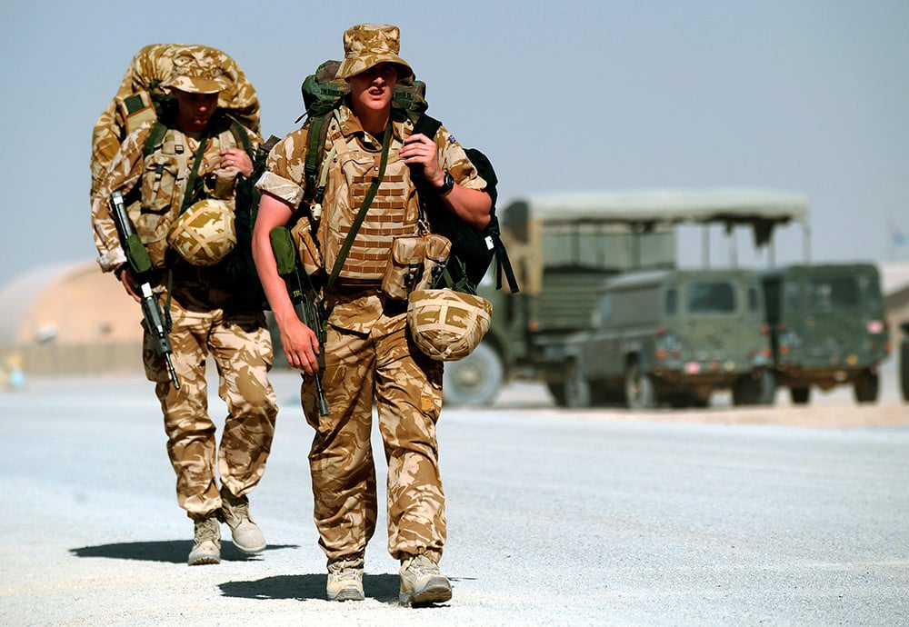Dos soldados británicos, con mochila al hombro, pasean por una base en Afganistán.   