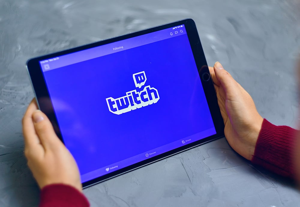 Unas manos sostienen una tableta en la que se puede ver el logo de Twitch sobre un fondo morado.