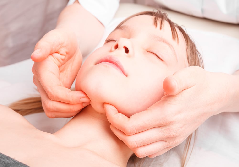 Fisioterapeuta realizando un masaje en el rostro de una niña afectada por una disfunción cráneo-mandibular.