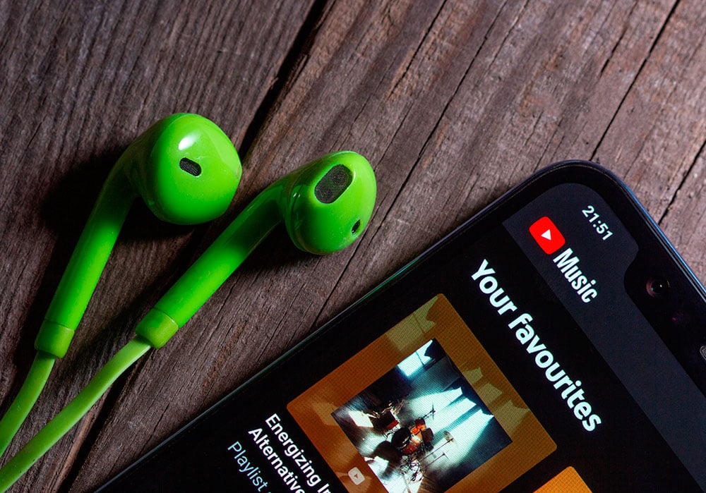 Aplicación de YouTube en un smartphone sobre una mesa de madera junto a unos auriculares de color verde. 