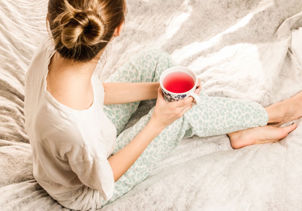 Mujer sentada sobre la cama sostiene un té rojo