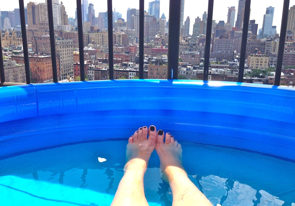 Imagen de unas piernas en una piscina hinchable situada en una terraza o balcón de un edificio en Nueva York