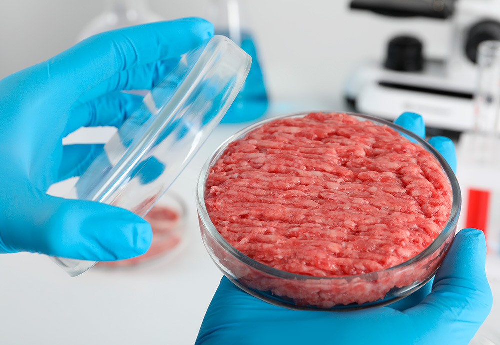 Imagen de un laboratorio en el que unas manos enguantadas manipula un trozo de carne cultivada. 