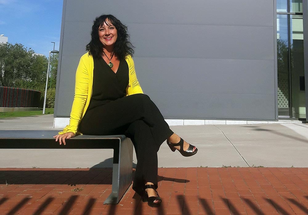 La profesora del grado en ADE de la UEMC Celia Martín, con chaqueta amarilla, sentada en un banco ubicado en el Campus de la UEMC