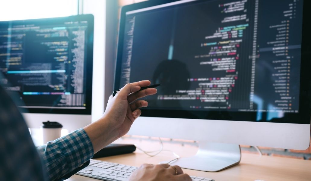 Mano de informático apunta a una pantalla con código de programación