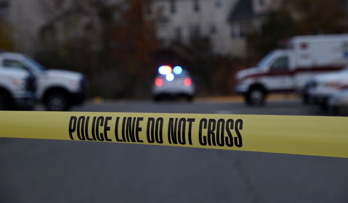 Cinta policial delimitando una escena acordonada con vehículos de emergencia al fondo.