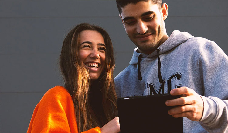 Dos estudiantes durante una Jornada de Puertas Abiertas sonríen mientras ven contenido en una tablet.