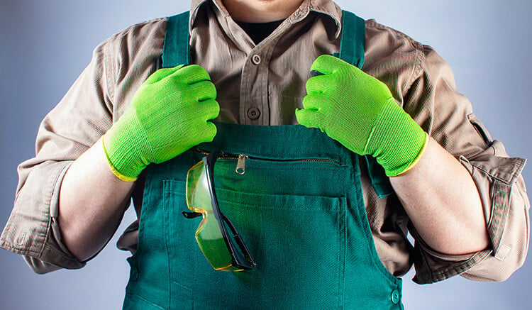 Torso de un hombre equipado con guantes de seguridad verdes y delantal del mismo color y camisa beige. 