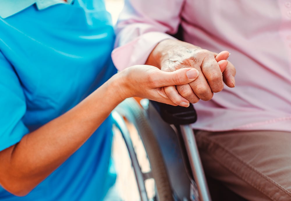 Una mano de una terapeuta ocupacional sostiene con cariño la mano de una anciana