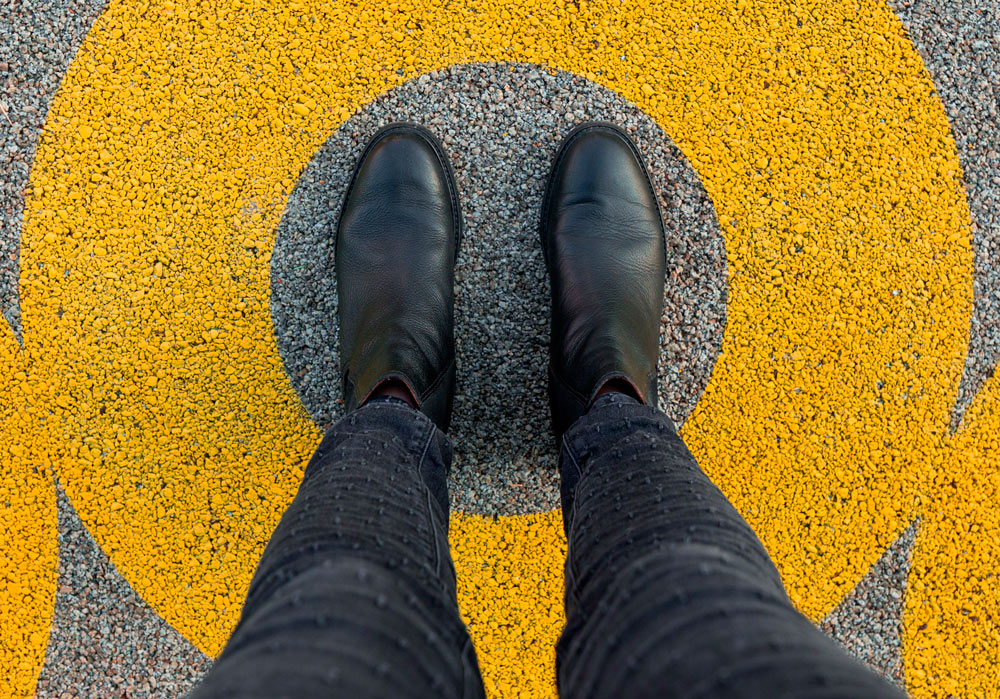 Pies de una chica con botines negros dentro de un círculo amarillo pintado en el pavimento como metáfora para describir la zona de confort