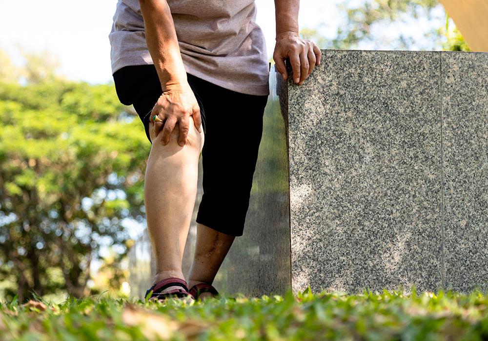Anciana aquejada de osteoporosis se sujeta una rodilla dolorida en un parque.
