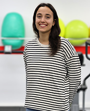 María Merino País, estudiante del Máster en Investigación en Actividad Física y Salud en Poblaciones Especiales, sonríe ante la cámara en un entorno de entrenamiento funcional, con material deportivo al fondo.